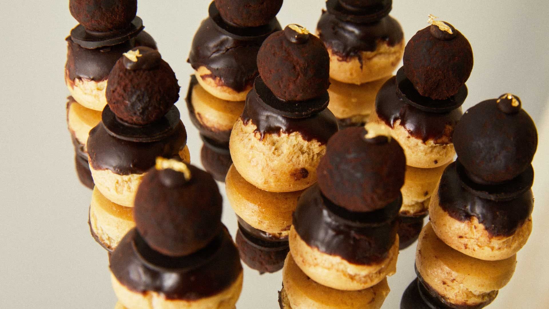 Çikolataya batırılmış profiterol kuleleri altın varak detaylarıyla üst üste dizilmiş.