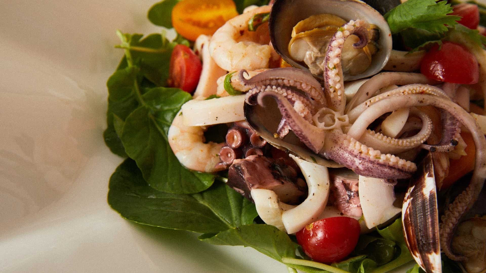 Ahtapot, karides, kalamar ve midyeden oluşan bir deniz mahsulleri salatası, kiraz domates ve marul yatağında.