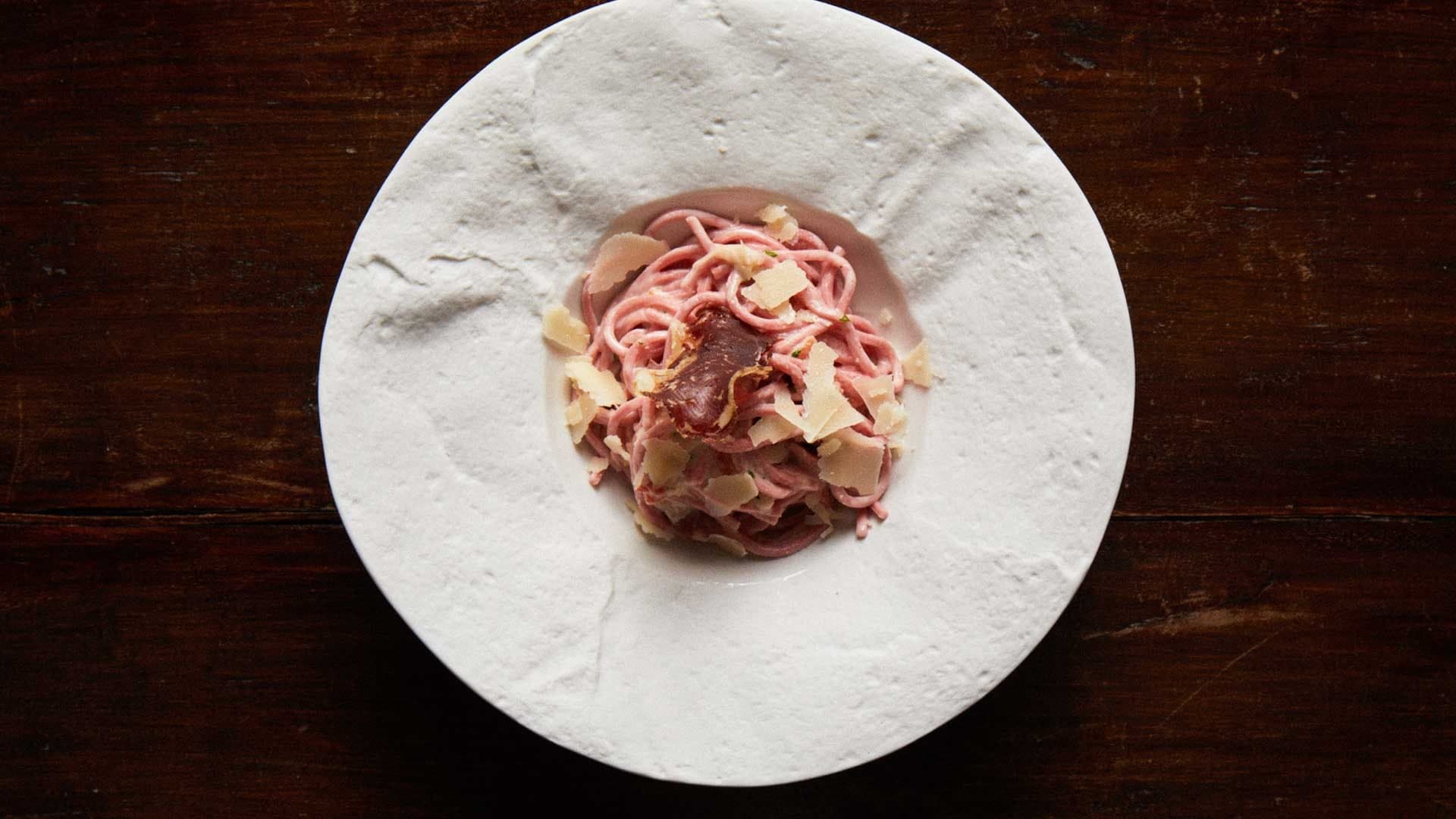 Pancar rengi spagetti üstten çekimde, parmesan tıraşlaması ve kıtır füme et dilimiyle süslenmiş.