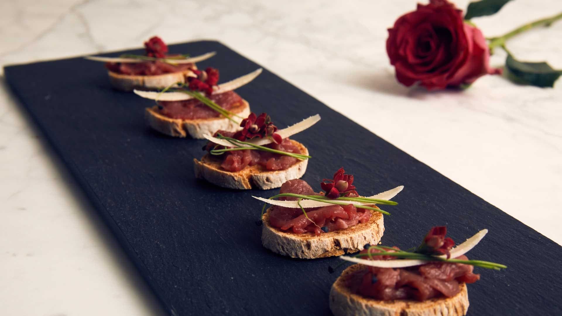 Kavrulmuş ekmek dilimi üzerine et tartarı ve parmesan tıraşlamasıyla sıra halinde dizilmiş kanepeler.
